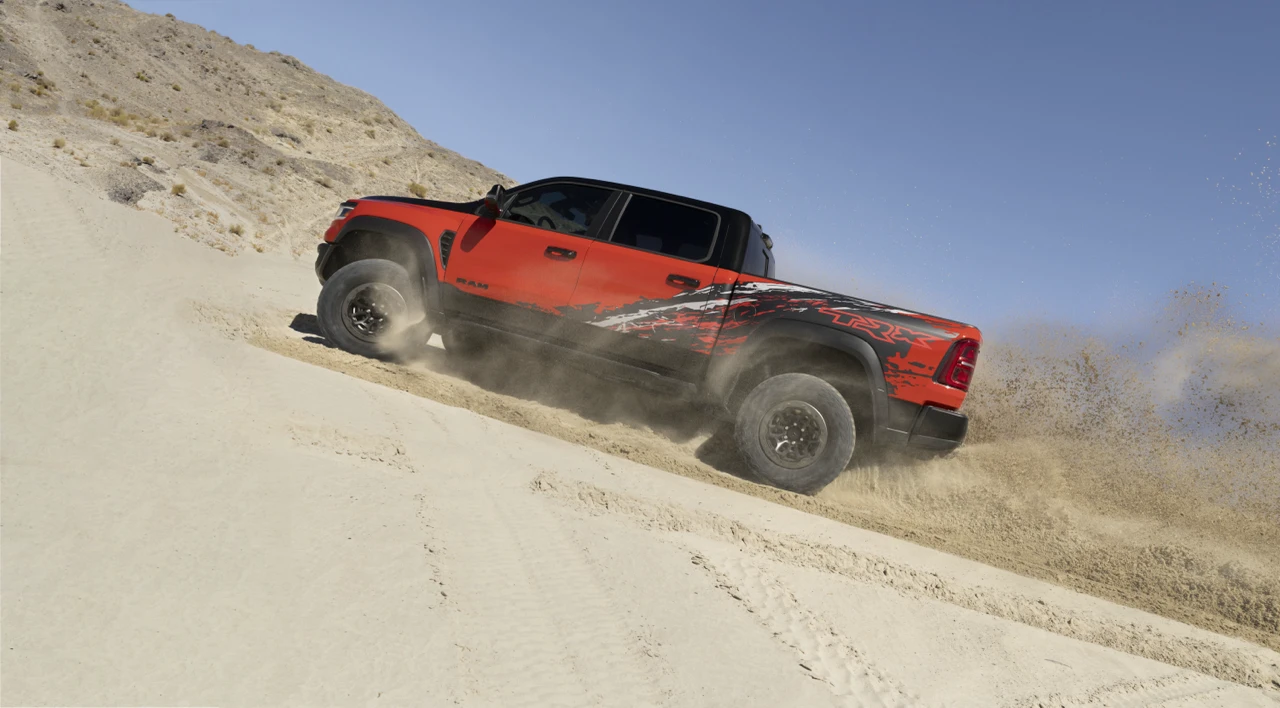 Red 2027 Ram 1500 SRT TRX climbing a sandy slope, showcasing its off-road capability.