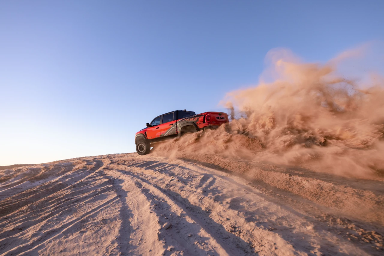 Red 2027 Ram 1500 SRT TRX driving up a sand dune and throwing a cloud of sand behind it.