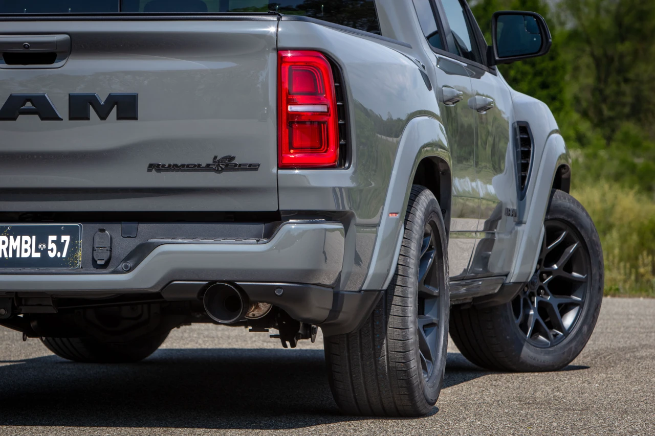 Rear three-quarter detail of a grey 2027 Ram 1500 Rumble Bee showing the tailgate, rear wheel and exhaust.