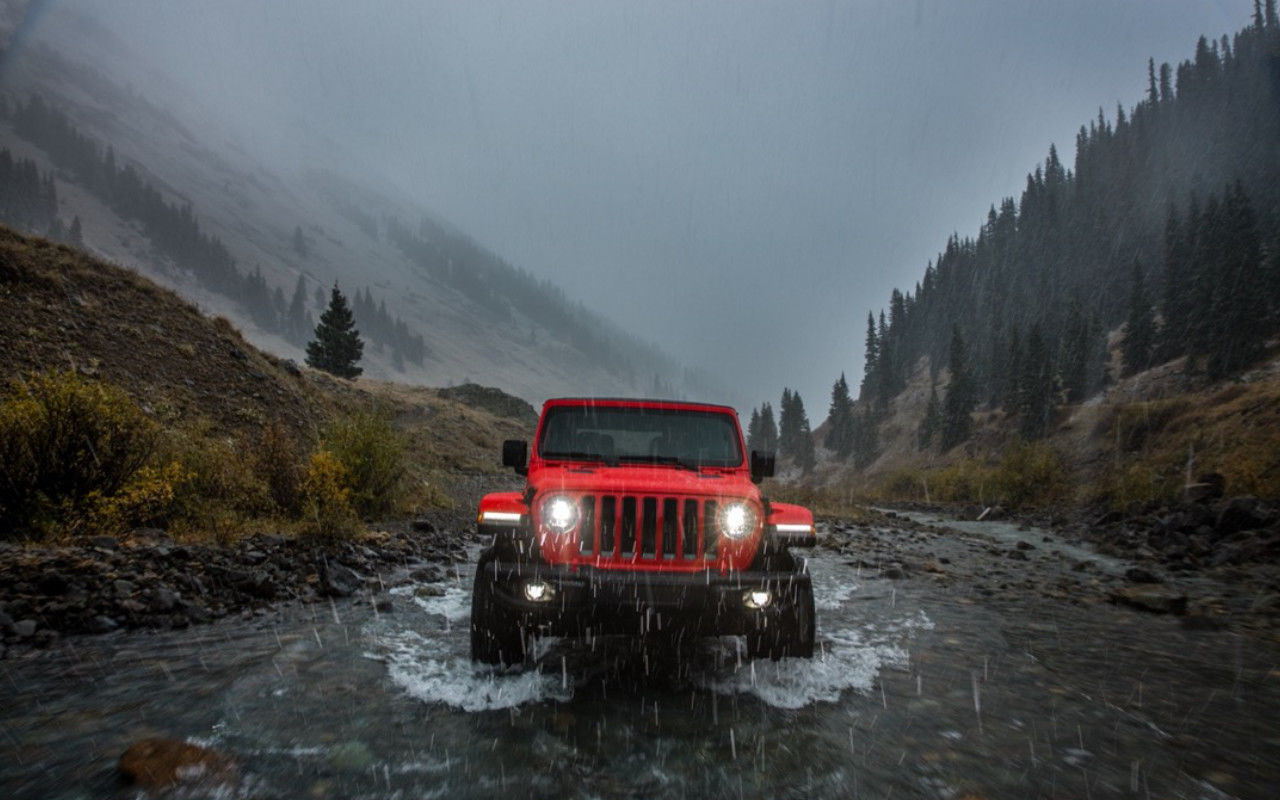 frontal view of a 2023 Jeep Wrangler driving through a stream in a valley