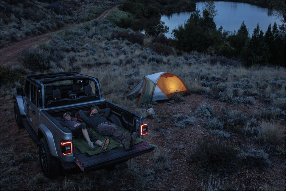 vue d'un couple couché dans la boite d'un Jeep Gladiator 2023 près de leur encampement à la tombée de la nuit