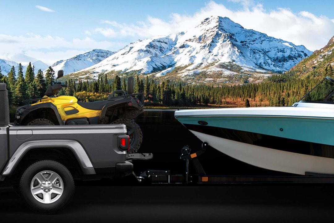 close up view of a 2023 Jeep Gladiator carrying an ATV and towing a boat in nature