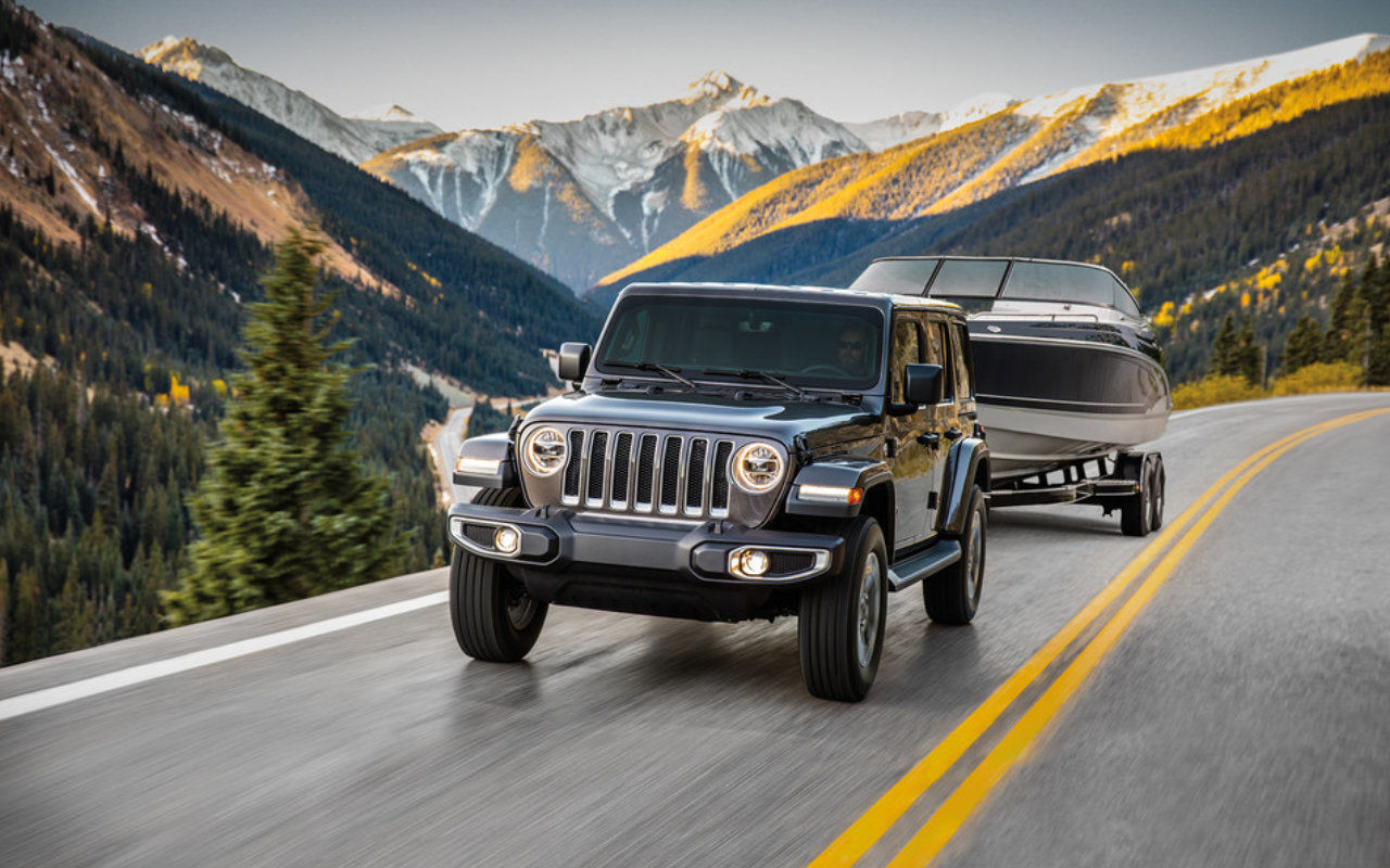 front side view of a 2023 Jeep Wrangler 4xe towing a boat on a mountain road