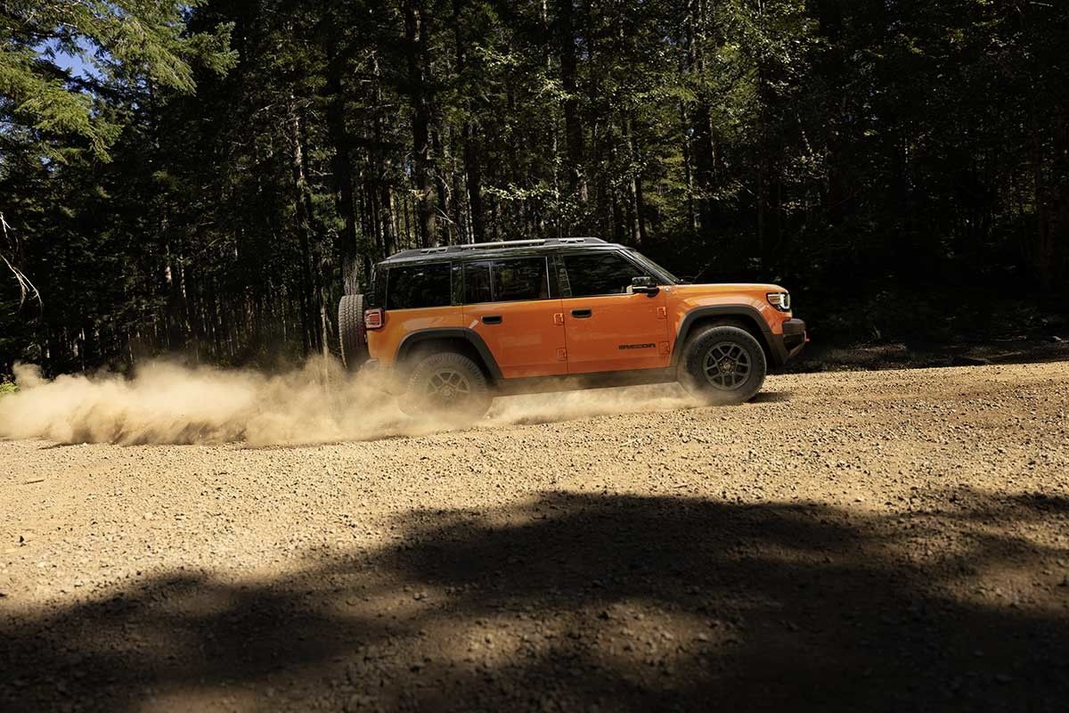 Jeep Recon 2026 orange en conduite hors route sur chemin de gravier, poussi&egrave;re soulev&eacute;e, vue de profil.
