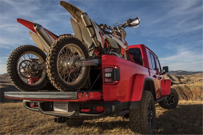 Un Jeep Gladiator qui roule dans l'herbe avec 2 motos chargées en arrière.