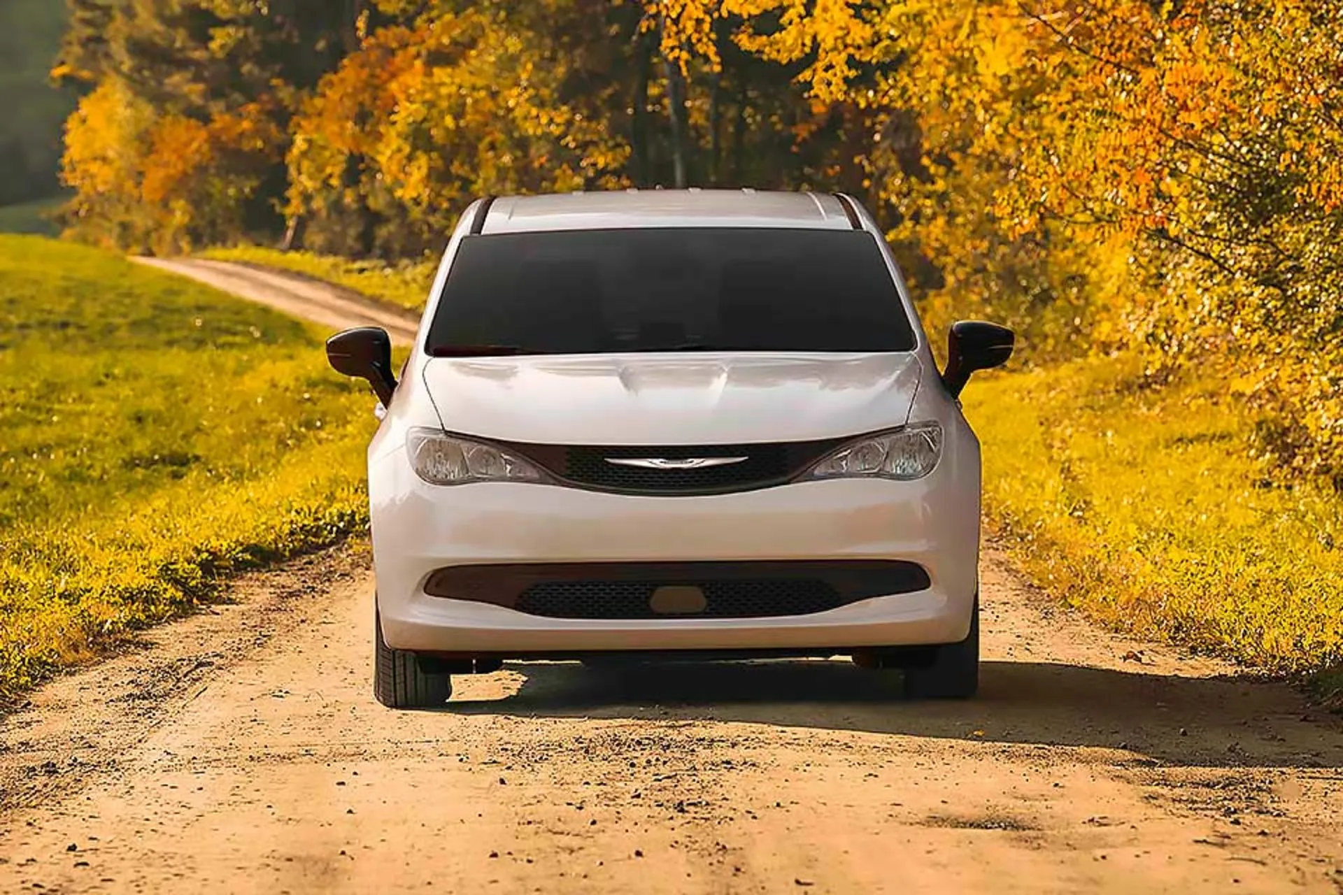 White 2026 Chrysler Grand Caravan front view on a country road lined with autumn trees.