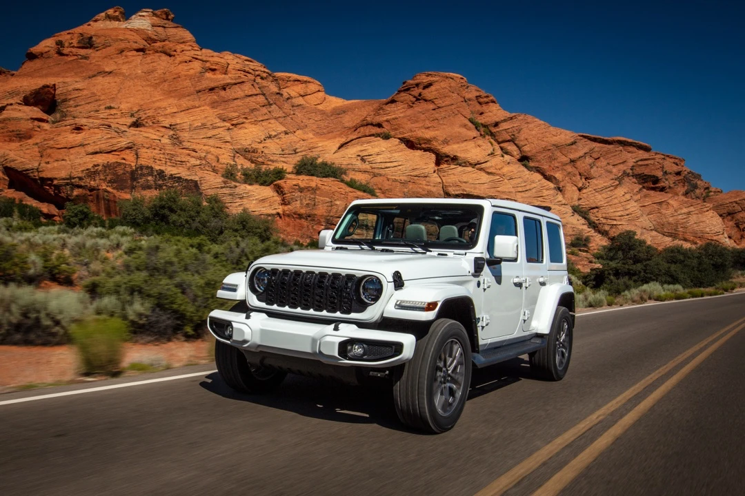 White 2025 Jeep Wrangler 4xe driving on a desert road.