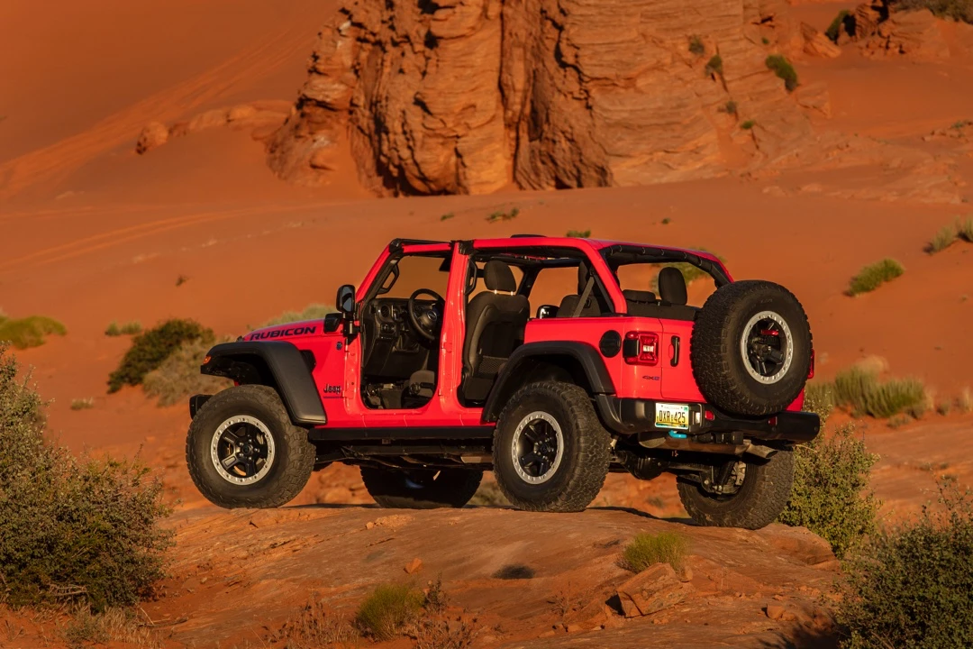 Red Jeep Wrangler Rubicon without doors on rocky terrain.