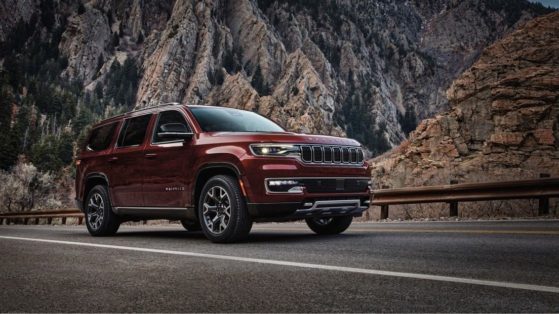 Le jeep Grand Wagoneer stationné sur la route devant une montagne.