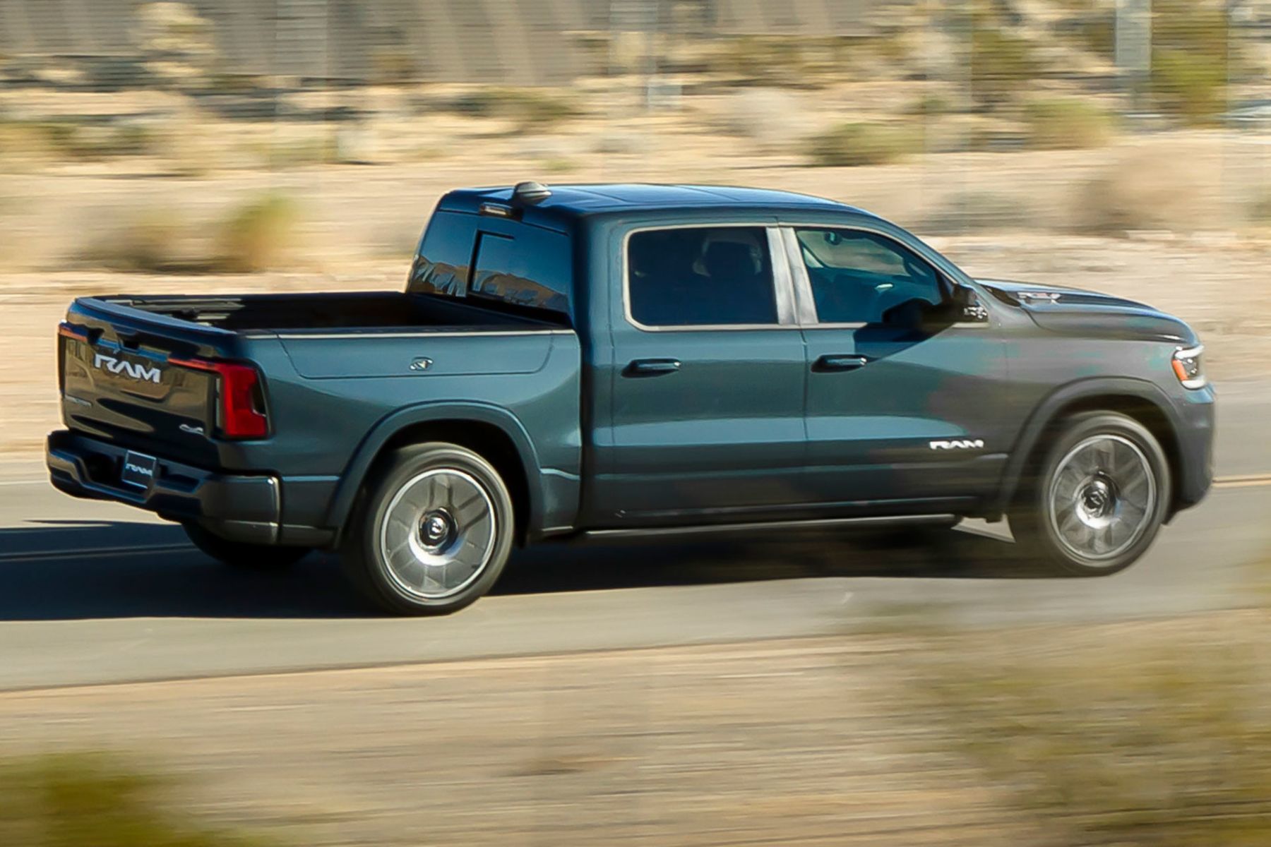 Green 2026 RAM 1500 Ramcharger driving on a desert road, side profile view.

