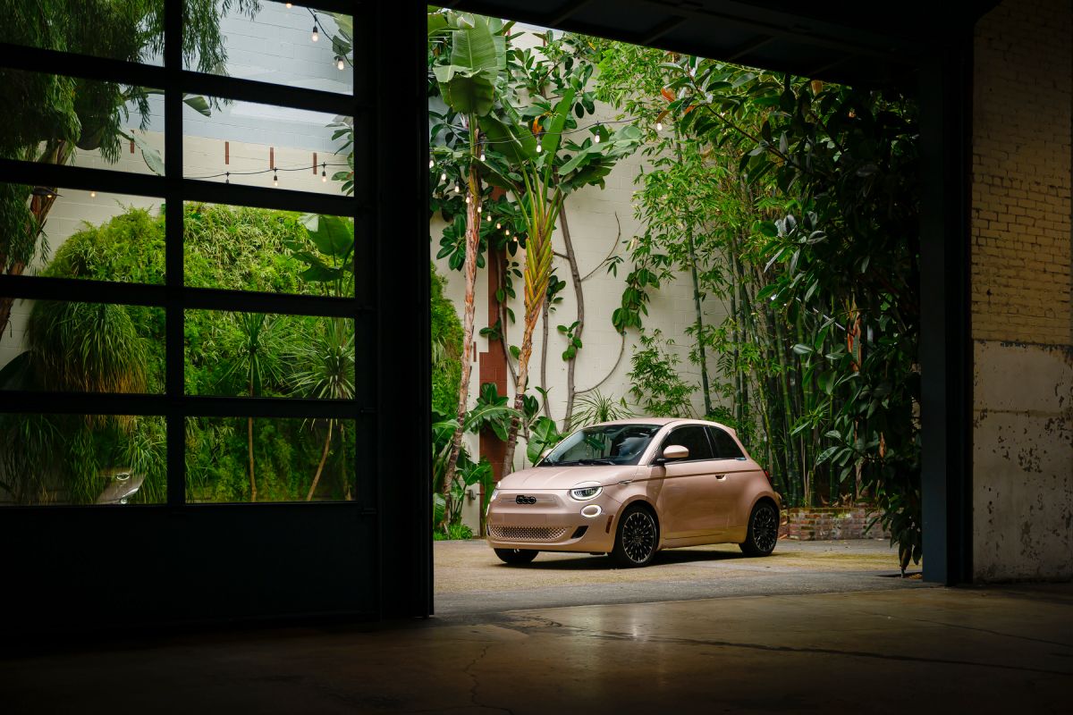 Beige 2025 Fiat 500e front view parked inside an industrial building surrounded by greenery.