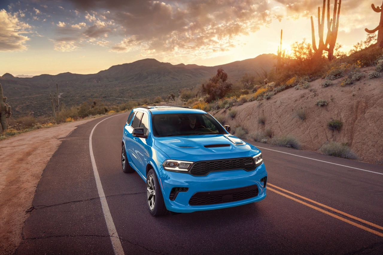 Blue 2026 Dodge Durango front view driving on a desert road at sunset.