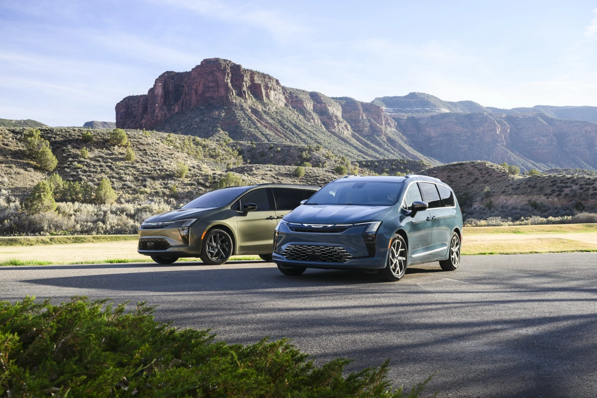 Two 2027 Chrysler Pacifica minivans in front of a mountain landscape.