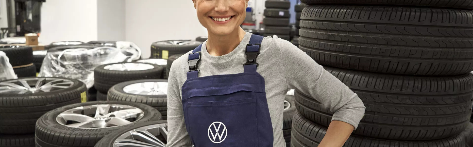 Un technicien VW sourit devant une pile de pneus
