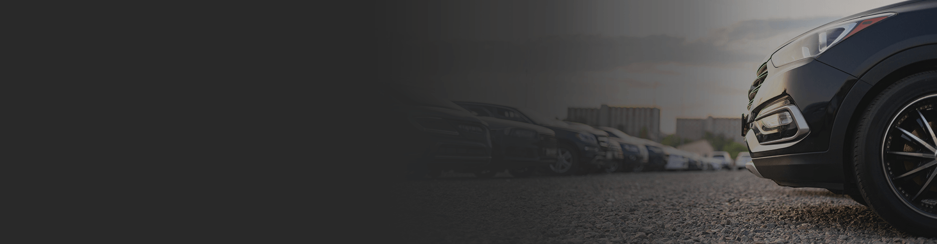 Row of parked cars at sunset with a close-up on a black SUV's wheel.