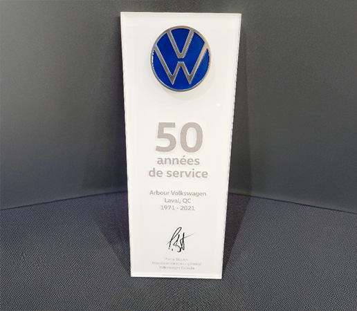 Trophée de reconnaissance en acrylique blanc orné du logo bleu de Volkswagen au sommet. L'inscription souligne « 50 années de service » pour Arbour Volkswagen à Laval, couvrant la période de 1971 à 2021, et porte la signature du président-directeur général de Volkswagen Canada.