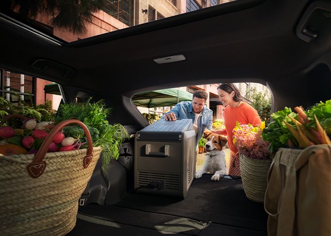 A smiling man sits in the driver's seat of a modern car, looking at his smartphone.