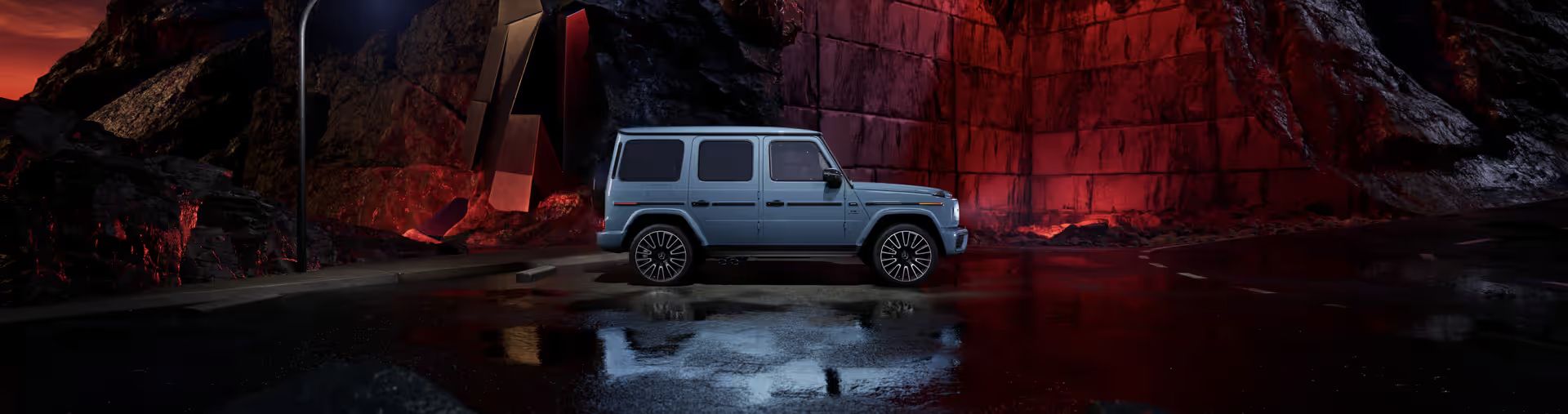 A profile shot of a slate-blue Mercedes-Benz G-Class SUV parked on a wet, reflective road at night.