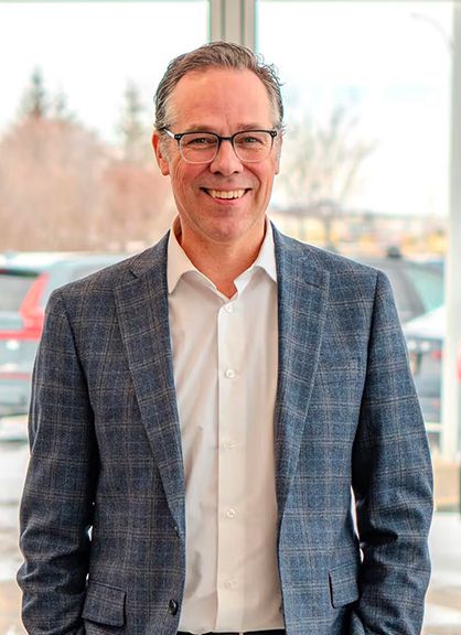 A smiling man in a blazer and glasses standing in a bright showroom.