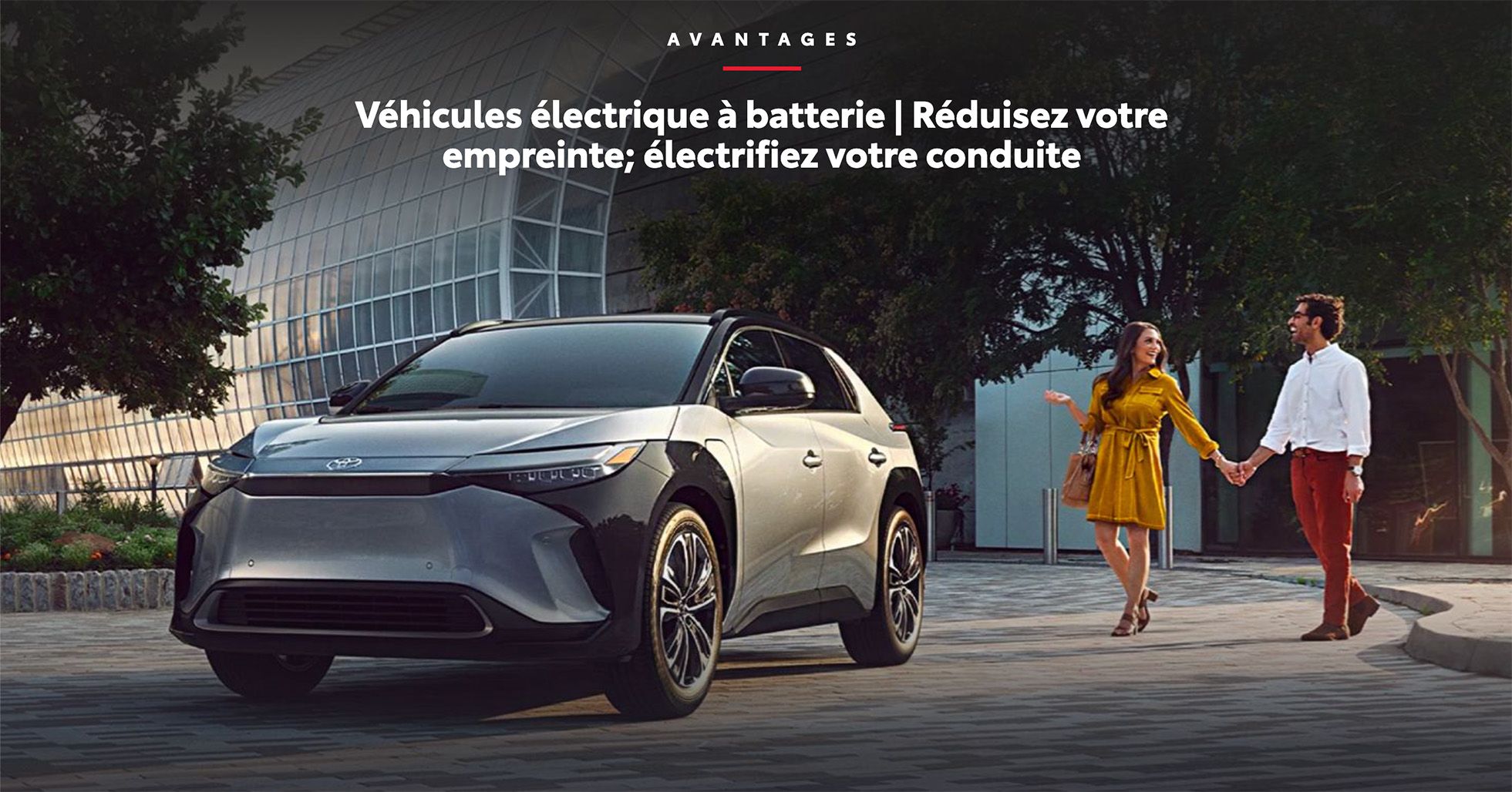 Couple marchant à côté d'un VUS électrique à batterie (Toyota bZ4X) devant un bâtiment moderne. Texte: Véhicules électrique à batterie | Réduisez votre empreinte; électrifiez votre conduite.