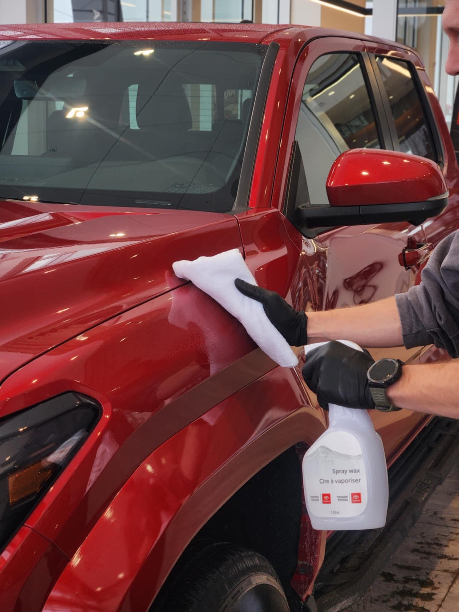 Technicien appliquant de la cire sur la carrosserie rouge d'un véhicule dans le centre d'esthétique Alma Toyota.