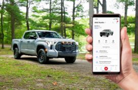 Main tenant un téléphone avec l'écran d'une application Toyota, et un pick-up Toyota Tundra en arrière-plan.