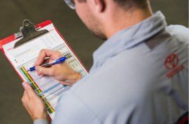 Technicien de service écrivant sur un presse-papiers avec un logo Toyota sur son uniforme.  Export to Sheets