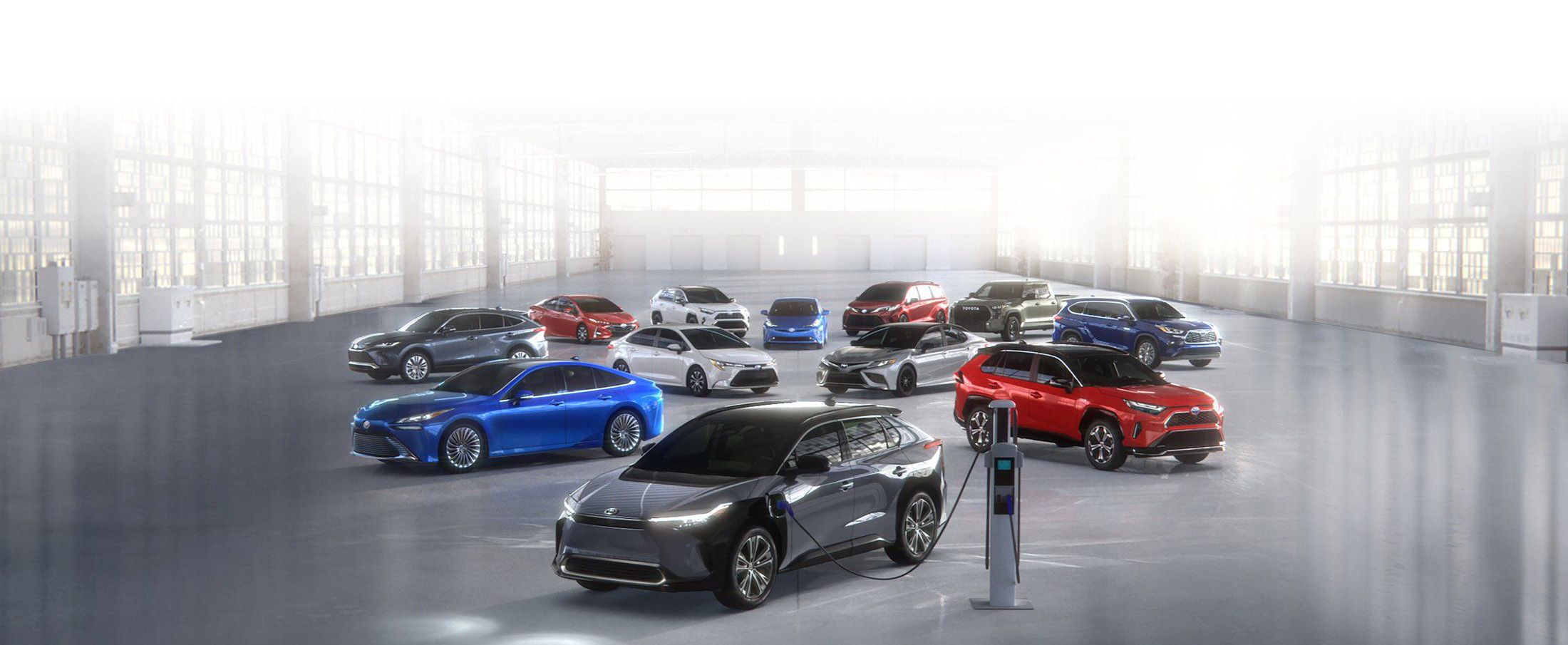Un ensemble de 10 véhicules électrifiés Toyota (hybrides, rechargeables, à batterie et à hydrogène) garés dans un entrepôt lumineux.