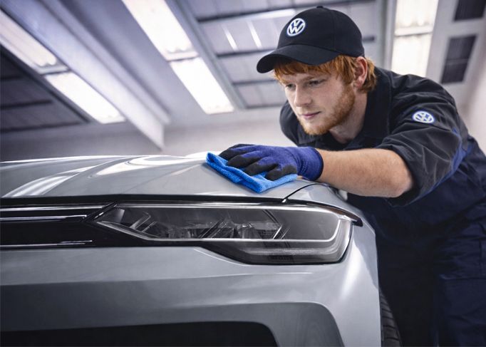 Smiling man wearing a red blazer, standing in a car dealership showroom.