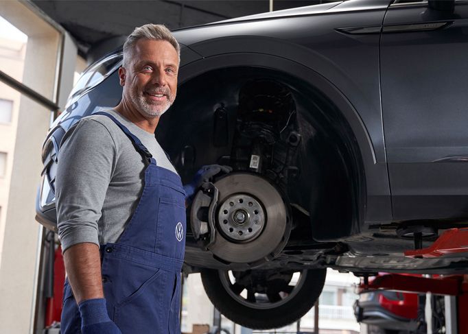 Smiling man wearing a red blazer, standing in a car dealership showroom.