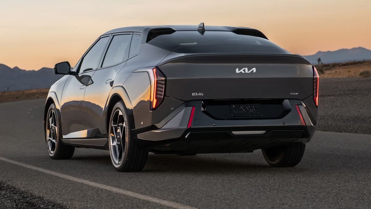 A red sedan is parked on a mountain road, with a large rocky cliff in the background.