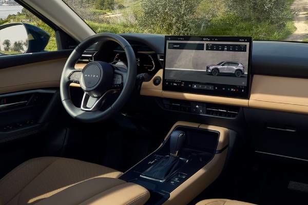 A red sedan is parked on a mountain road, with a large rocky cliff in the background.