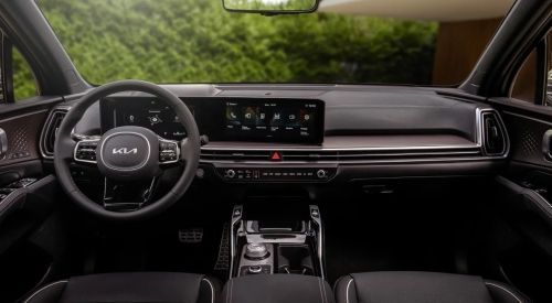 A smiling man sits in the driver's seat of a modern car, looking at his smartphone.