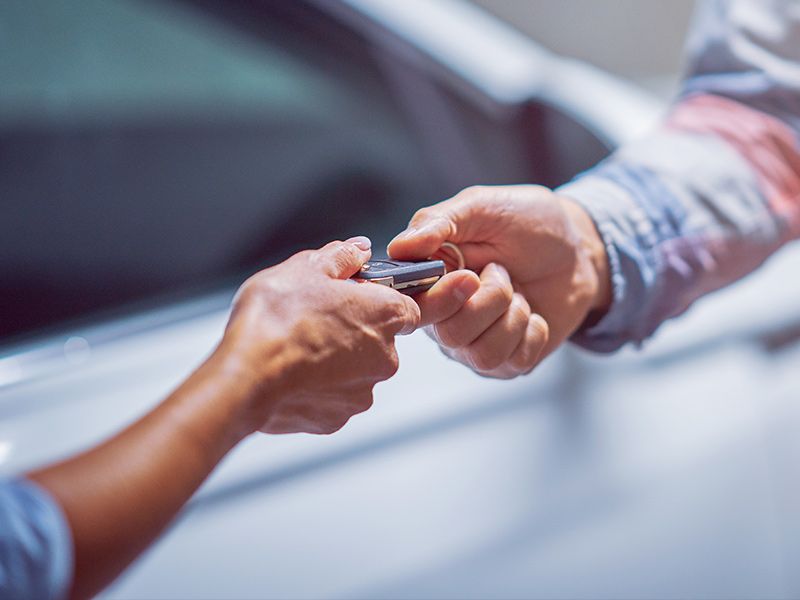 A smiling man sits in the driver's seat of a modern car, looking at his smartphone.