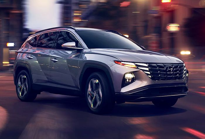 The rear view of a red sedan parked on the side of a rural road, with green hills in the distance.