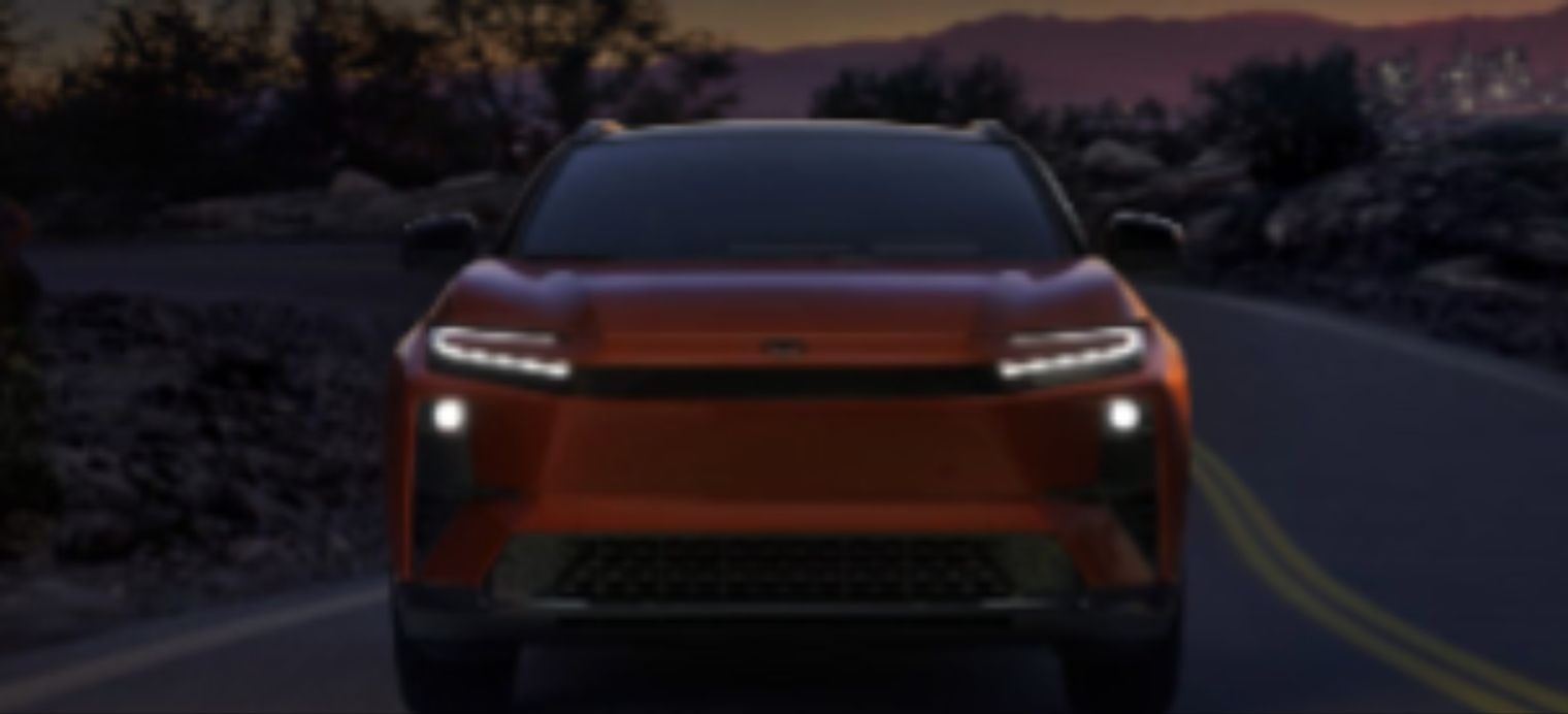 Une femme souriante se tient dans un concessionnaire automobile, regardant son téléphone intelligent tout en tenant un gobelet de café.