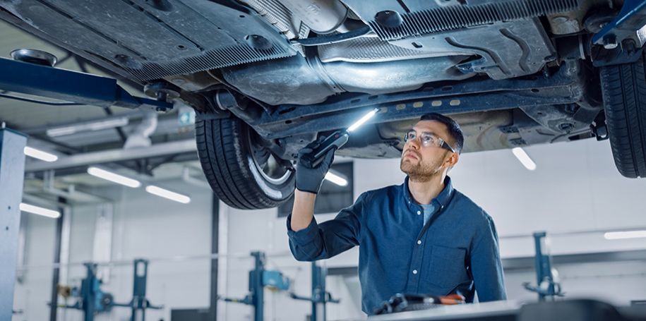 A mechanic using a flashlight to inspect the underside of a car on a lift.