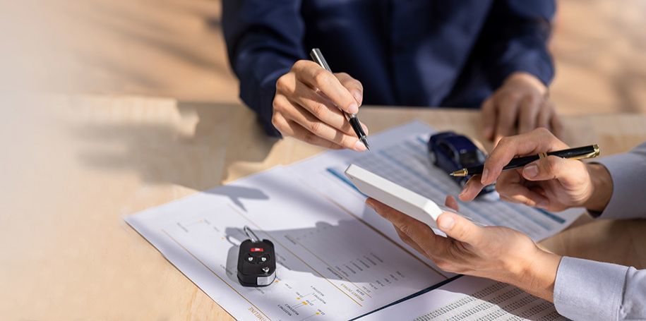 Gros plan de mains utilisant une calculatrice et signant des documents de financement automobile.