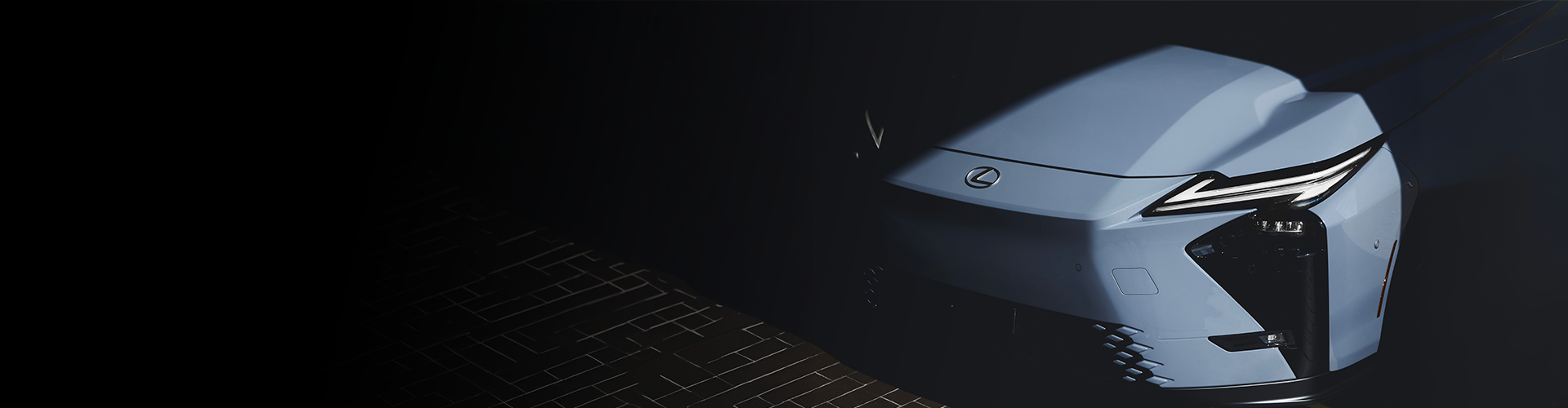 Un plan rapproché en plongée de l'avant d'un véhicule électrique Lexus bleu clair, mettant en valeur le design affûté de ses phares et son emblème sur un fond sombre.