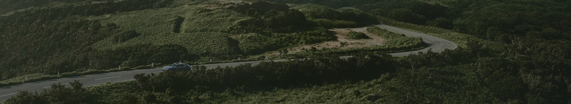 Une vue aérienne d'une Lexus roulant sur une route sinueuse à travers des collines verdoyantes.