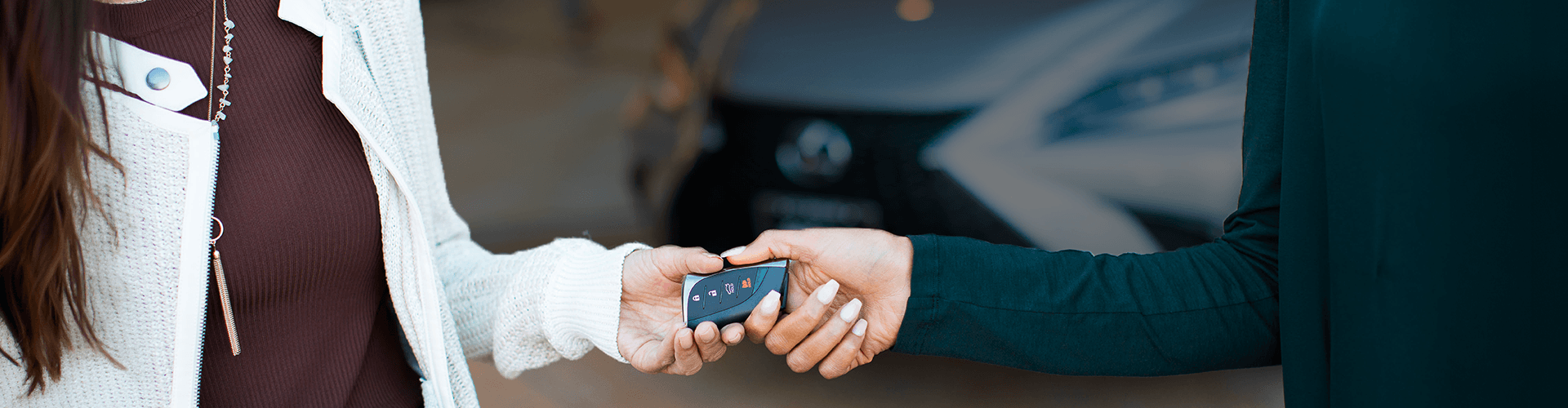 Un plan rapproché d'une personne remettant une clé électronique de voiture à une autre personne, avec un véhicule Lexus flouté en arrière-plan.