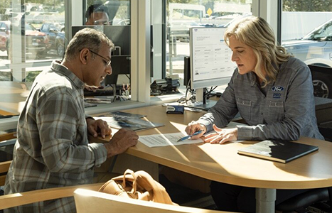 A Ford Pro representative at a dealership desk discussing financing paperwork with a customer.