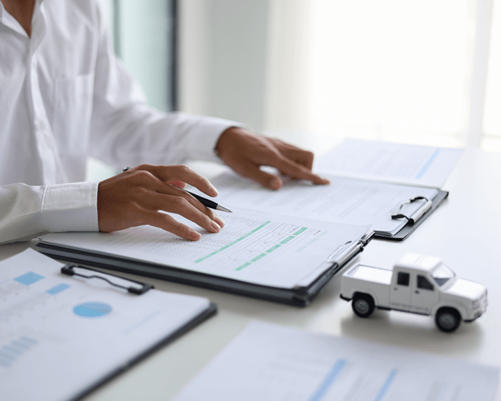 Gros plan d'une personne en chemise blanche examinant des documents financiers et des porte-blocs sur un bureau à côté d'un petit camion jouet blanc