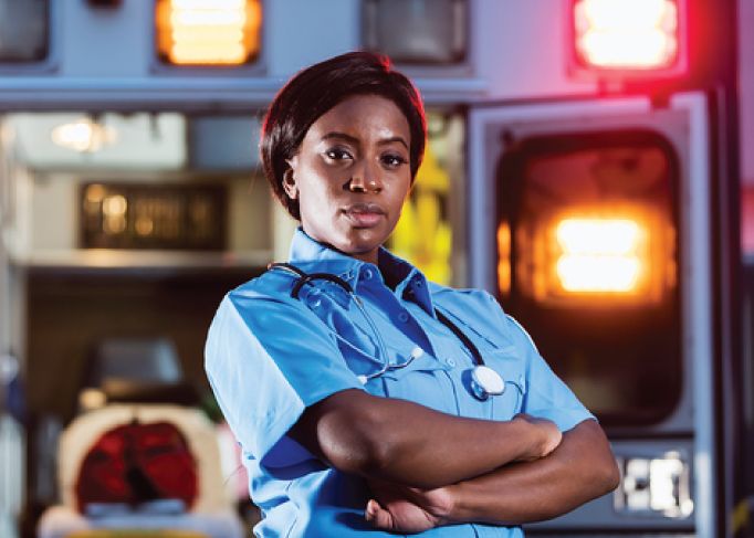 Smiling man wearing a red blazer, standing in a car dealership showroom.