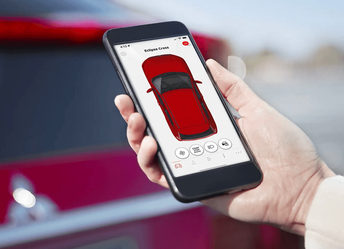 Une personne tenant un téléphone intelligent affichant l'application de télécommande Mitsubishi pour le « Eclipse Cross », avec un véhicule rouge flou en arrière-plan.