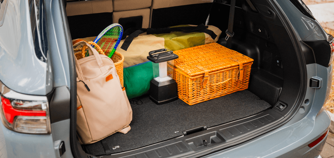 Le coffre ouvert d'un VUS gris rempli d'équipement de plein air, incluant un panier de pique-nique en osier, un sac à dos, des raquettes de tennis et une lanterne.