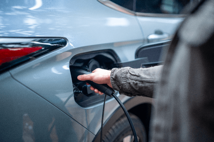 Gros plan d'une main branchant un câble de recharge dans le port latéral d'un véhicule Mitsubishi bleu clair.