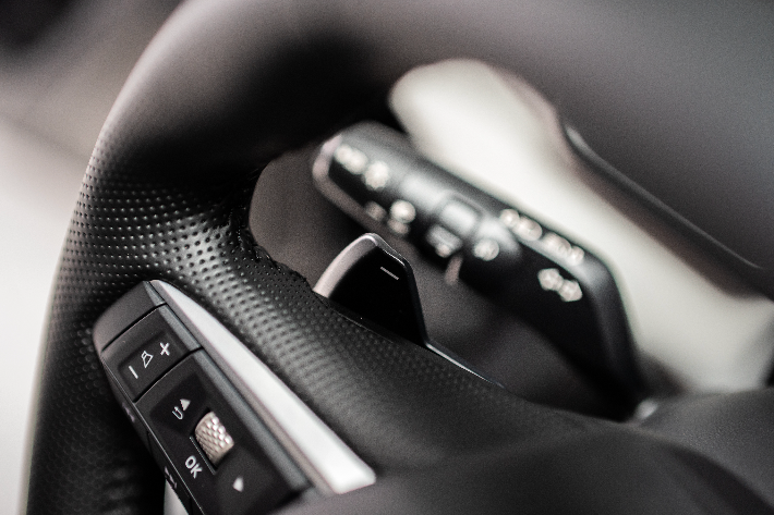 Vue détaillée de la poignée texturée du volant, comprenant des commandes audio intégrées et une palette de changement de vitesse argentée.