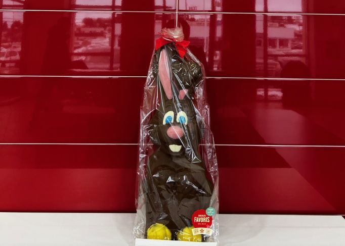Homme souriant portant une veste rouge, debout dans un concessionnaire automobile.