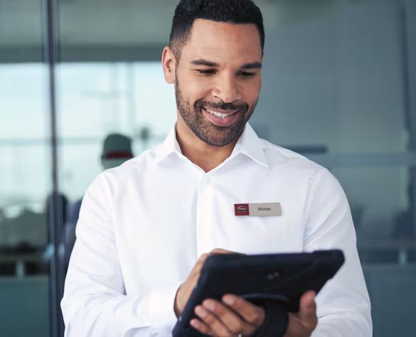 A smiling man named Michael wearing a white collared shirt and a name badge, looking down at a tablet he is holding.